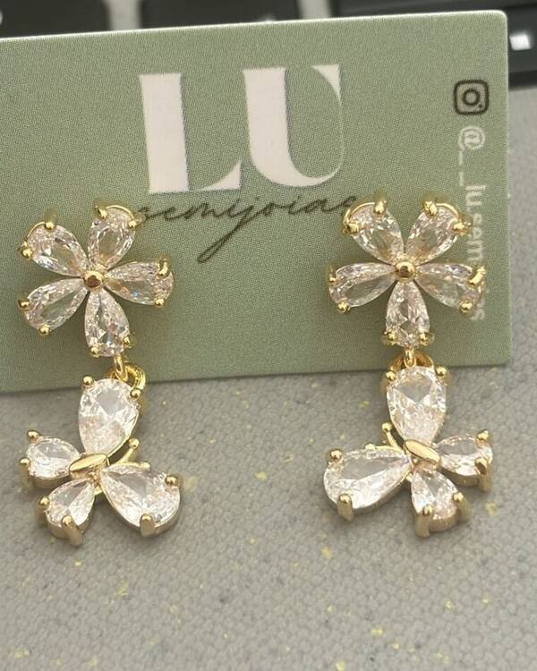 Brincos dourados de flor e borboleta com zircônias no cartão da Lu Semijoias
